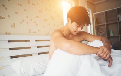 Man sitting in bed worried and shirtless